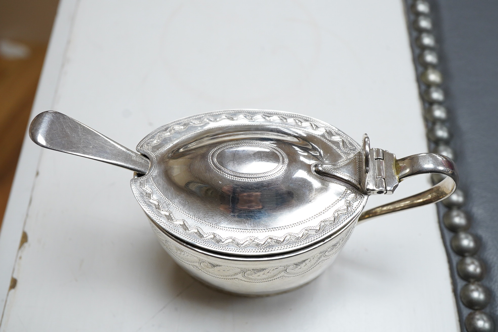 A George III engraved oval silver mustard pot, by James Mince, London, 1805, height 69mm, together with an associated silver mustard ladle, Thomas Dicks, London, 1808.